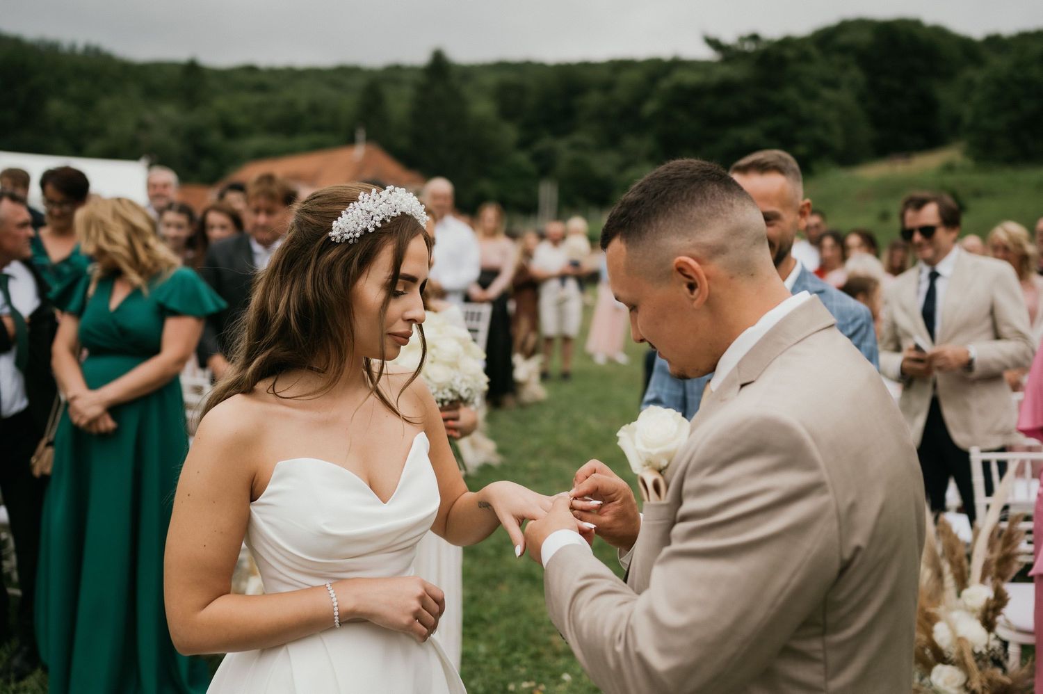 Wedding ceremony moment captured outdoors with guests in emerald dresses looking on.