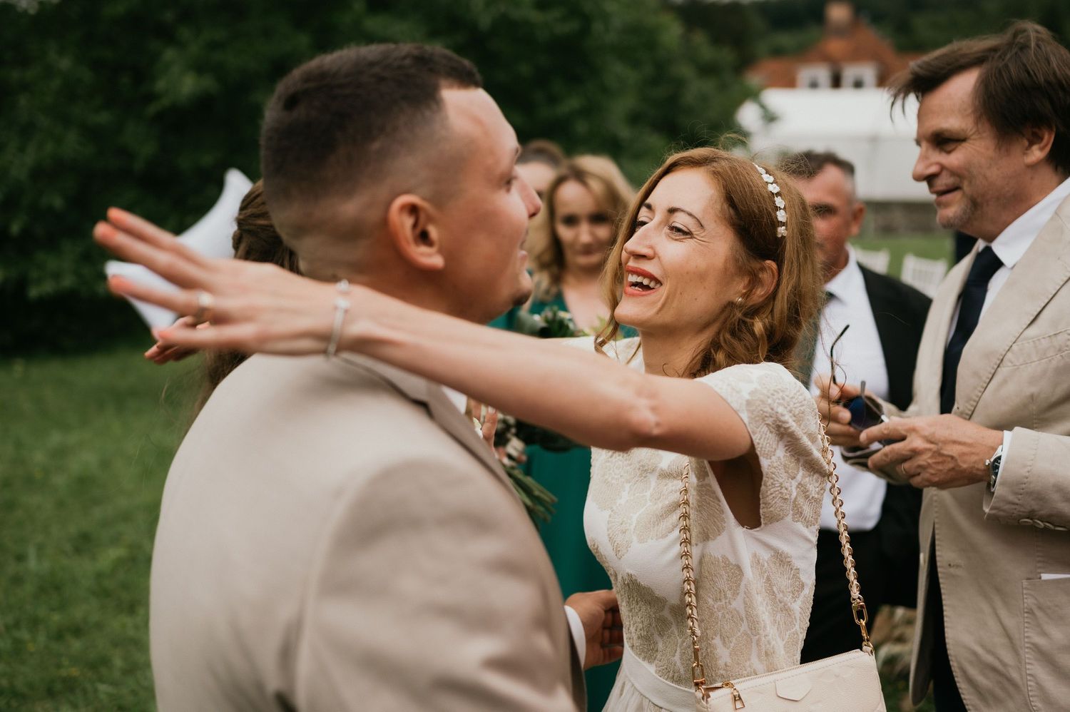 Newlyweds share a joyful moment during outdoor wedding reception with guests in background.