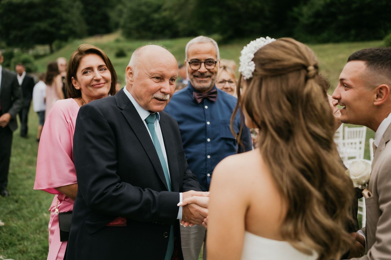 Wedding receiving line with guests greeting the bride in white dress outdoors.
