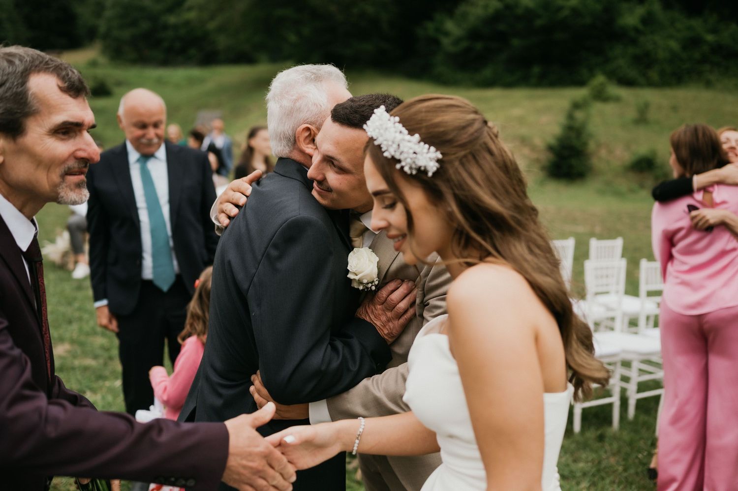 Wedding celebration showing warm greetings and embraces between guests and wedding party outdoors.