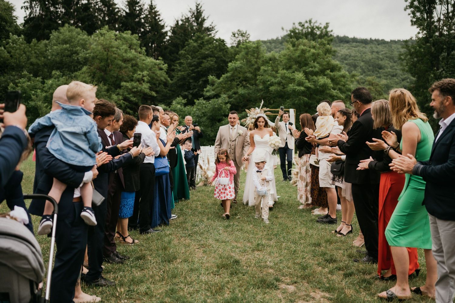 Wedding guests form aisle pathway outdoors as newlyweds walk through celebration.