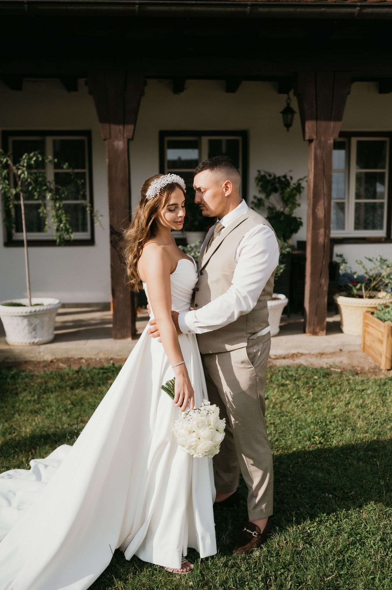 Romantic wedding portrait of couple in white and beige attire against rustic building exterior.
