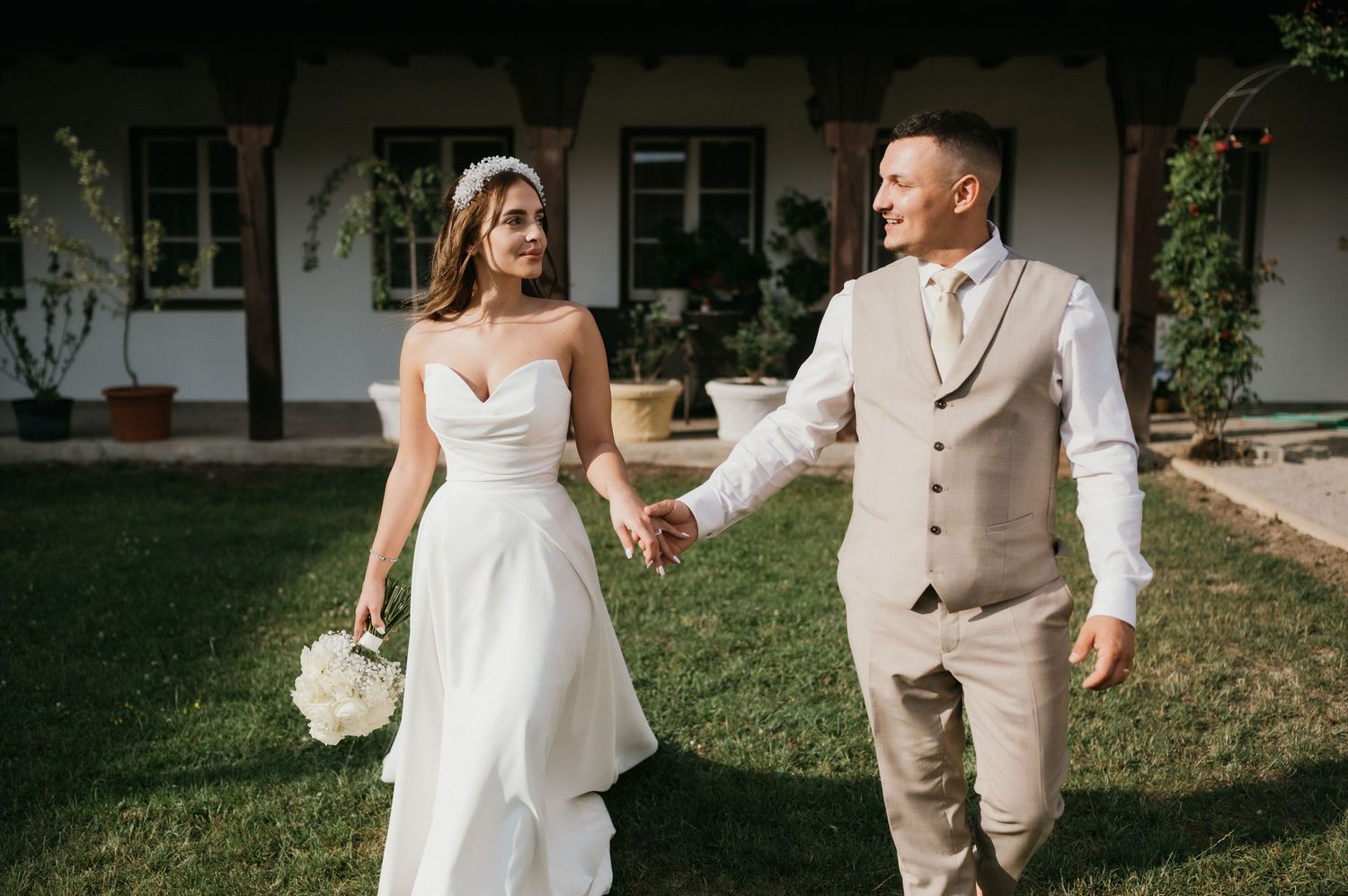 A couple shares a romantic moment in wedding attire on a lawn with a beautiful building backdrop.