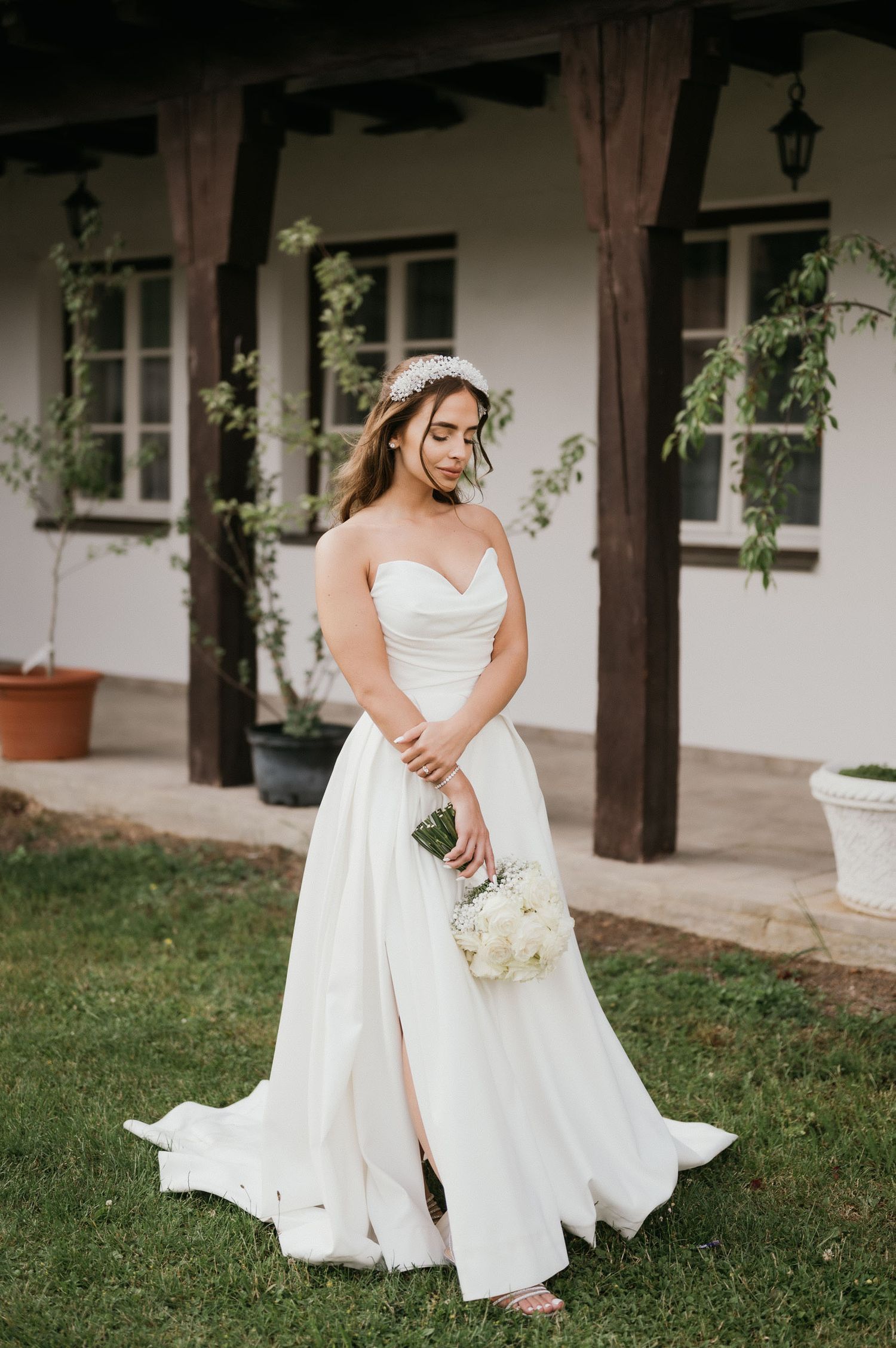A bride in a flowing white dress poses on grass holding a bouquet of white roses.