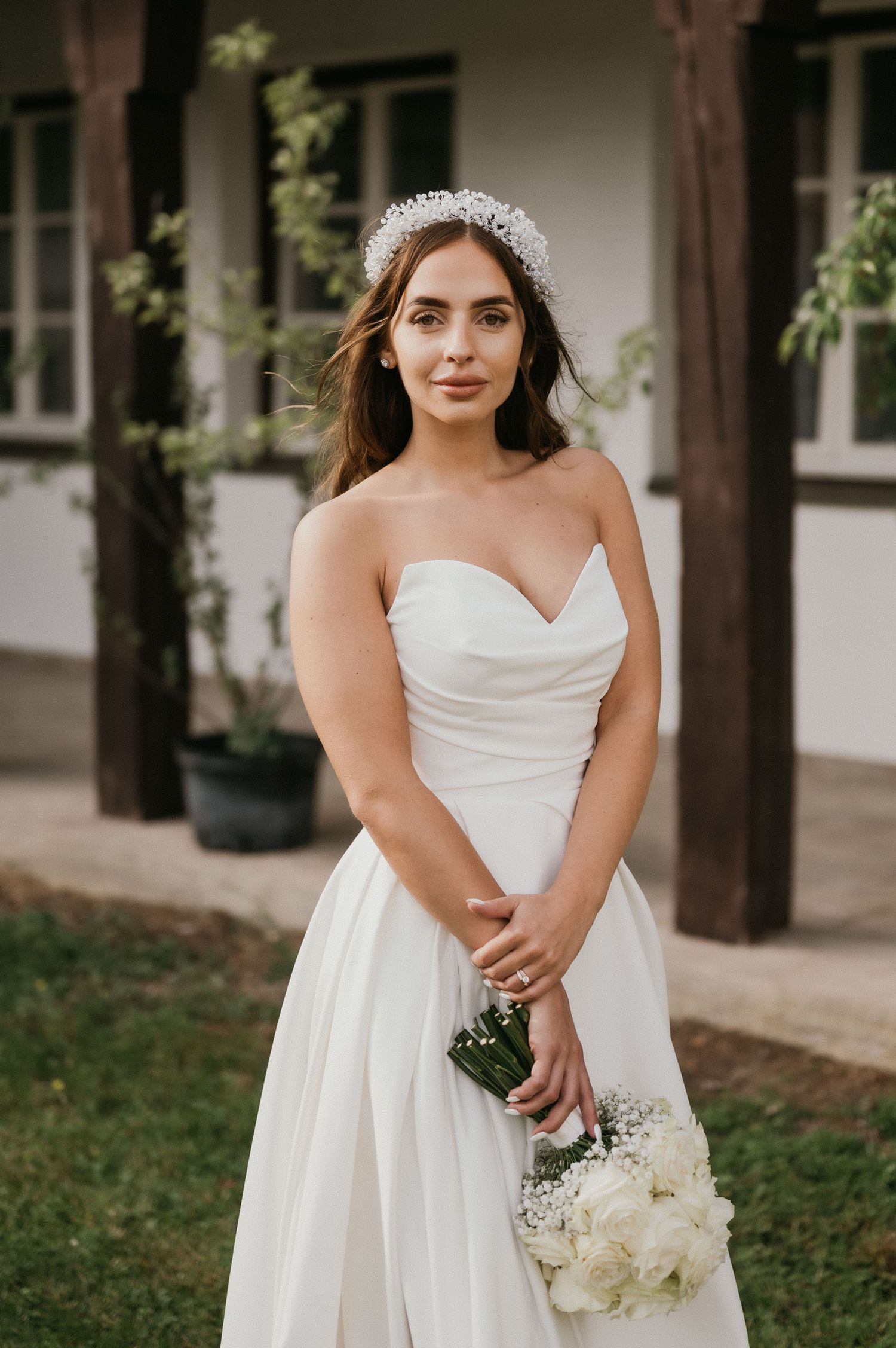 Portrait of a bride in a sweetheart neckline dress holding a white bouquet against white walls.