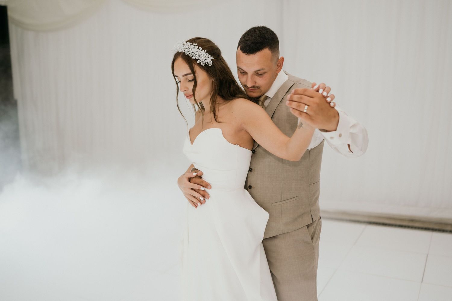 Couple shares intimate dance moment surrounded by fog effects at indoor wedding reception.
