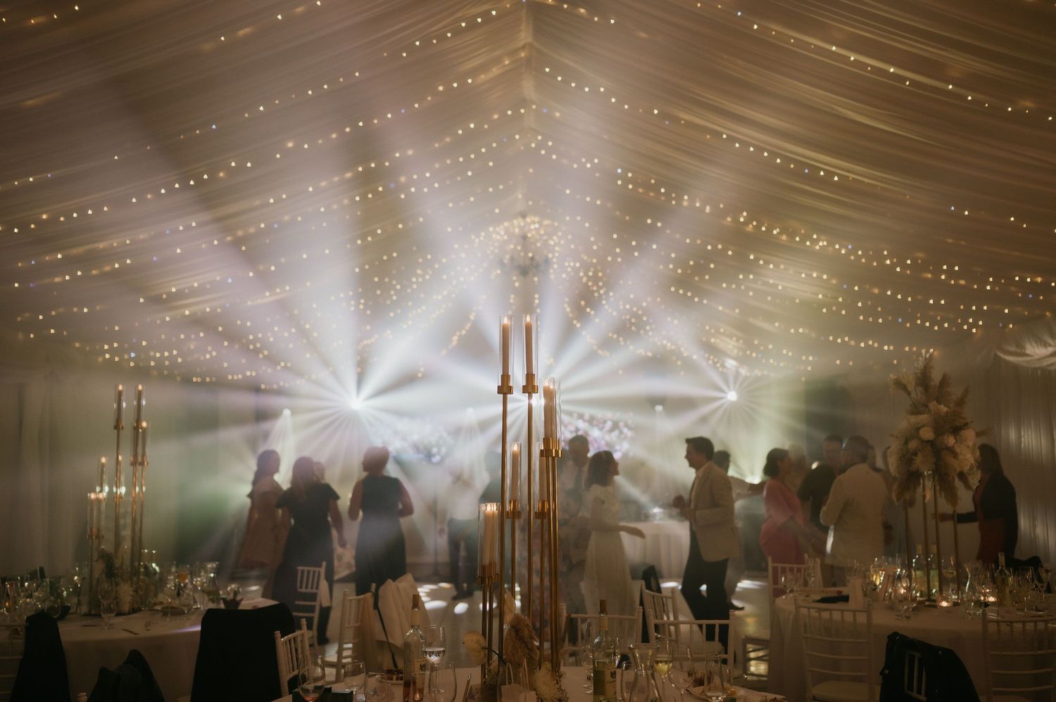 Wedding reception tent lit with magical string lights and beams creating ethereal atmosphere.