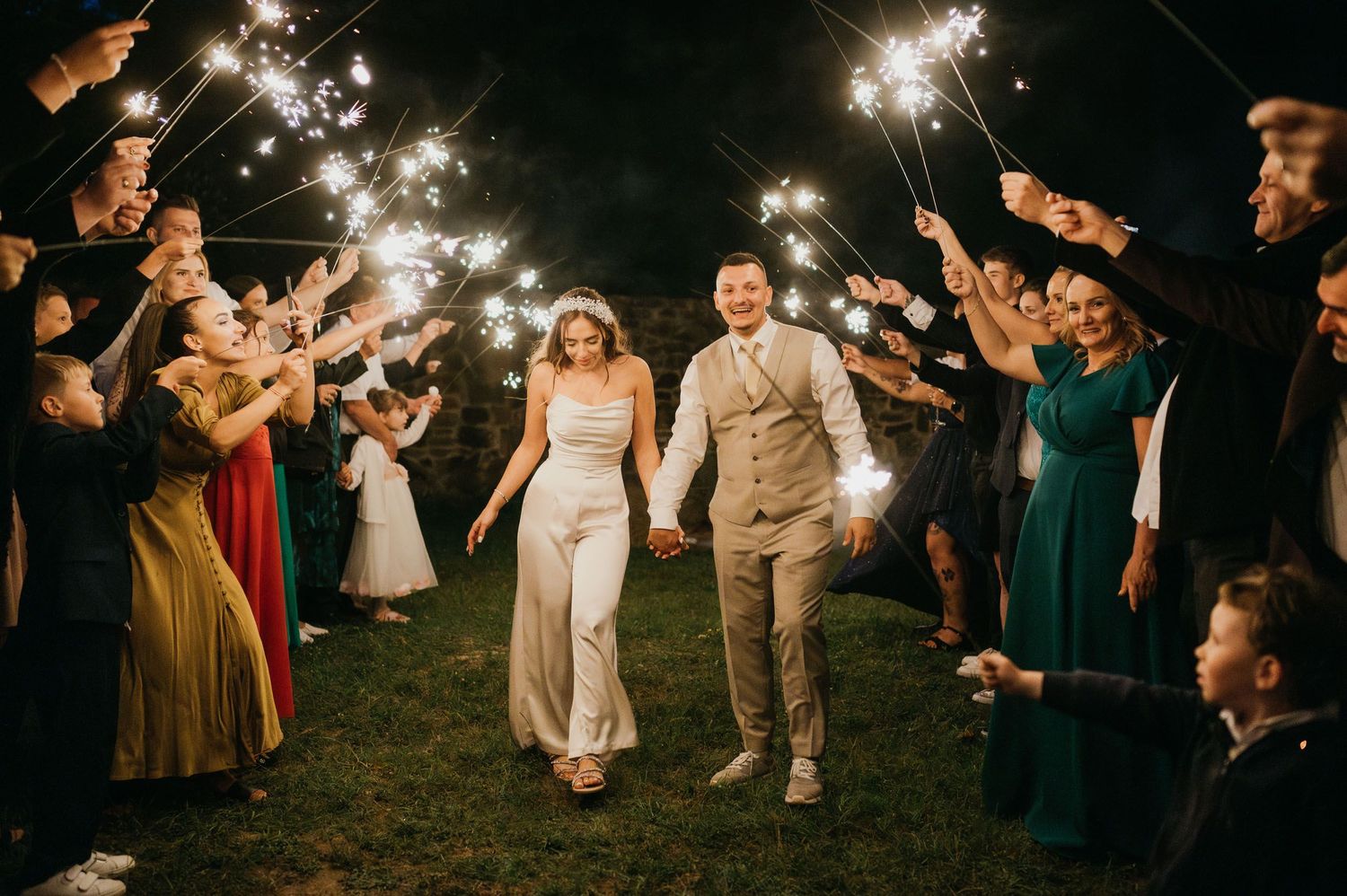 Wedding guests form sparkler tunnel exit for bride and groom in evening celebration.