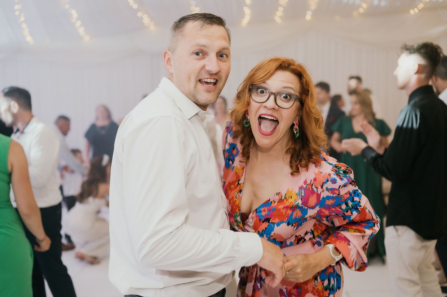 Wedding guests dancing and celebrating on a lively dance floor under string lights.