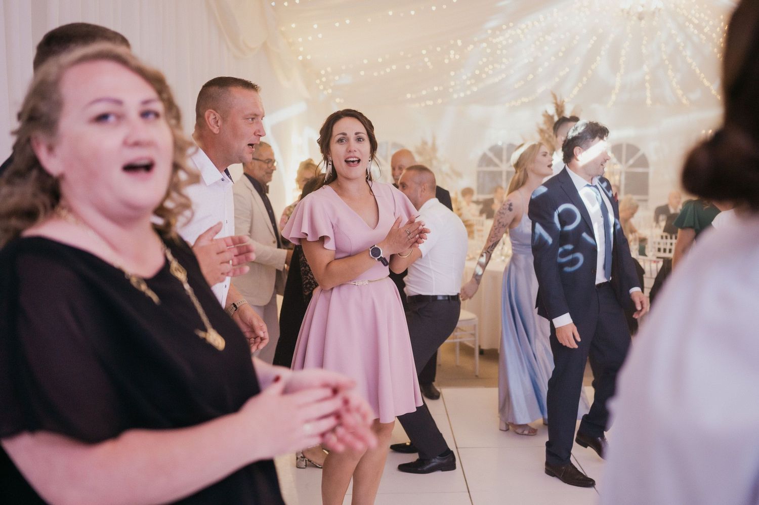 Wedding reception guests dancing and enjoying themselves on a white dance floor.
