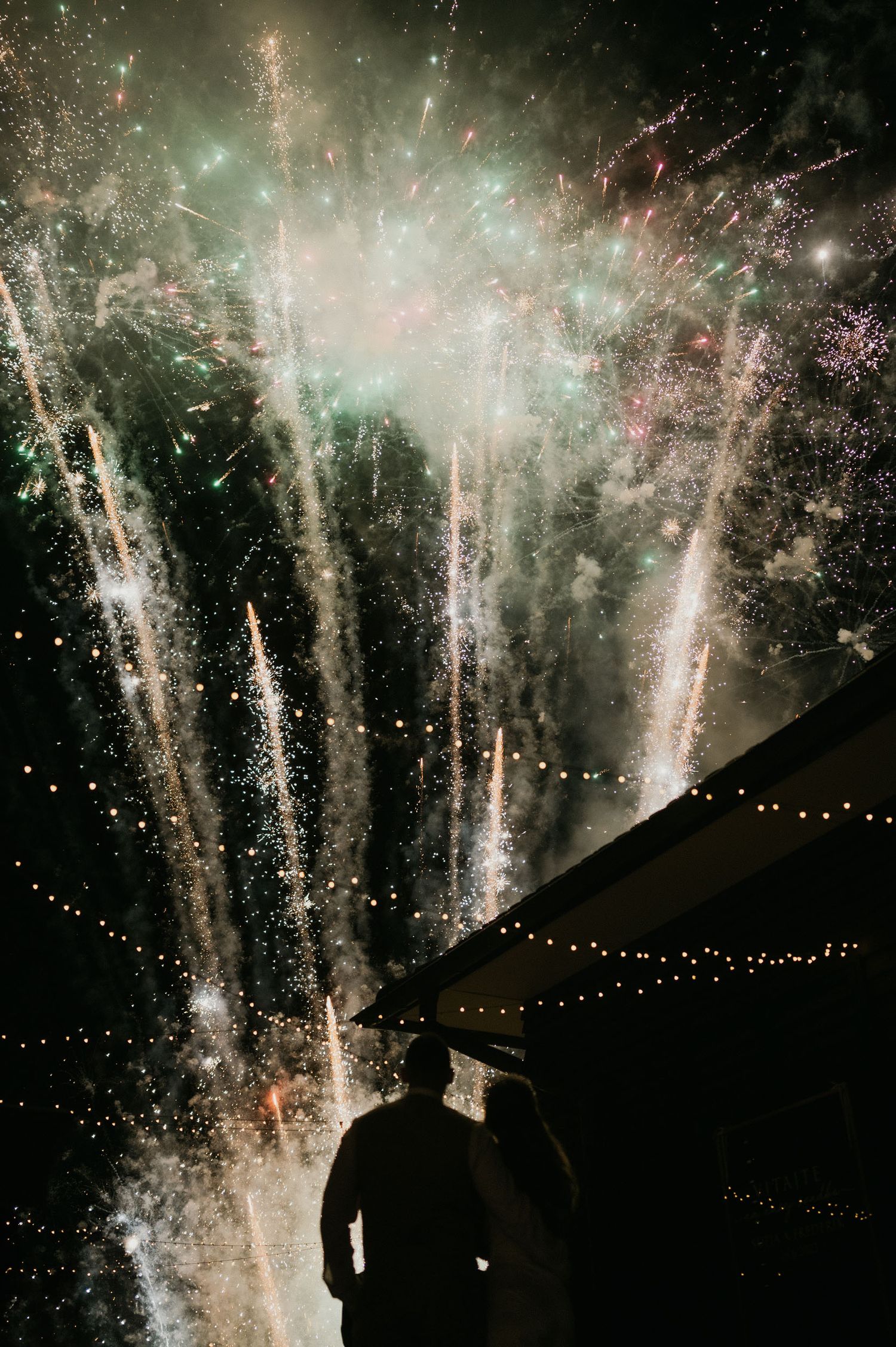 Dramatic fireworks display lighting up the night sky over a tent with string lights.