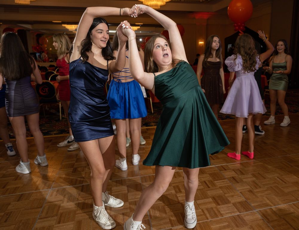 Two dancers in formal dresses perform energetic dance moves on a parquet floor at a party event.