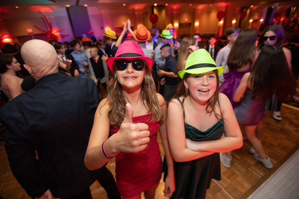 Party guests wearing colorful hats and dancing under red ambient lighting.