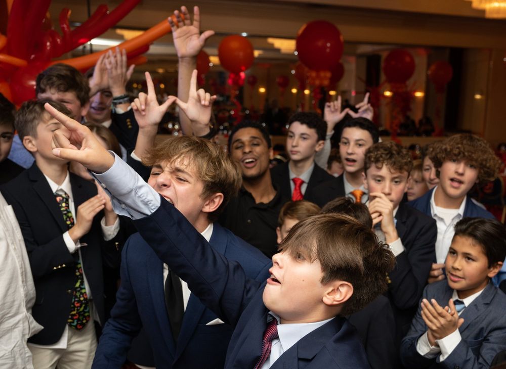 Enthusiastic crowd cheering with raised hands at indoor celebration with red balloon decorations.