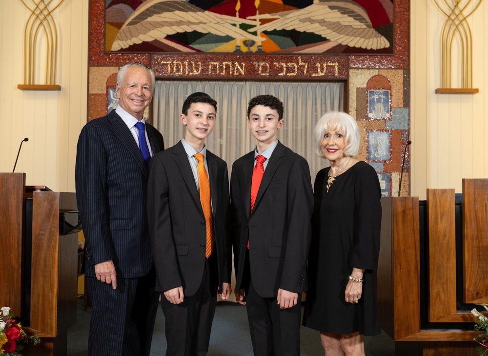 A formal group portrait taken in front of a synagogue altar with Hebrew text.