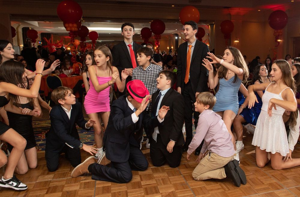 Dancers in formal wear performing synchronized moves on a wooden dance floor with red decorations.