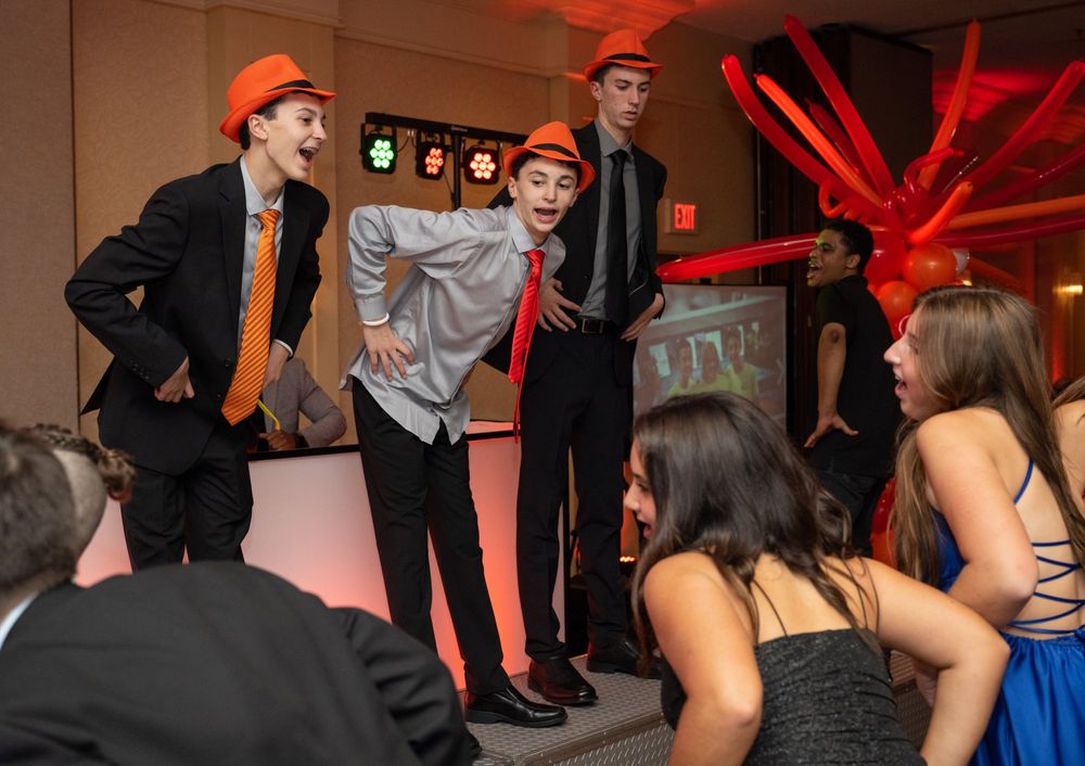 Dancers in formal wear performing for seated guests at indoor party with red lighting.