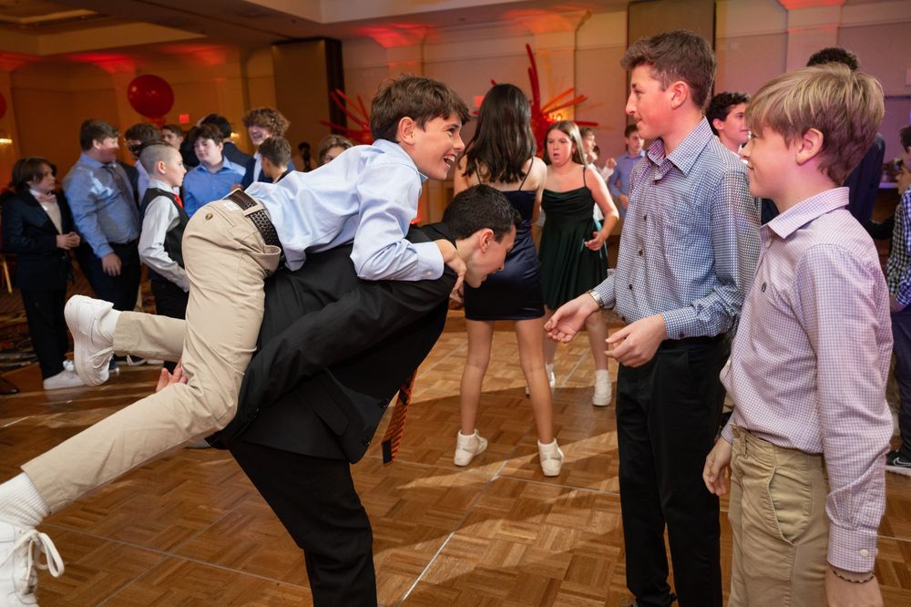 Energetic dance moves being performed by attendees at a formal party with red decorations.