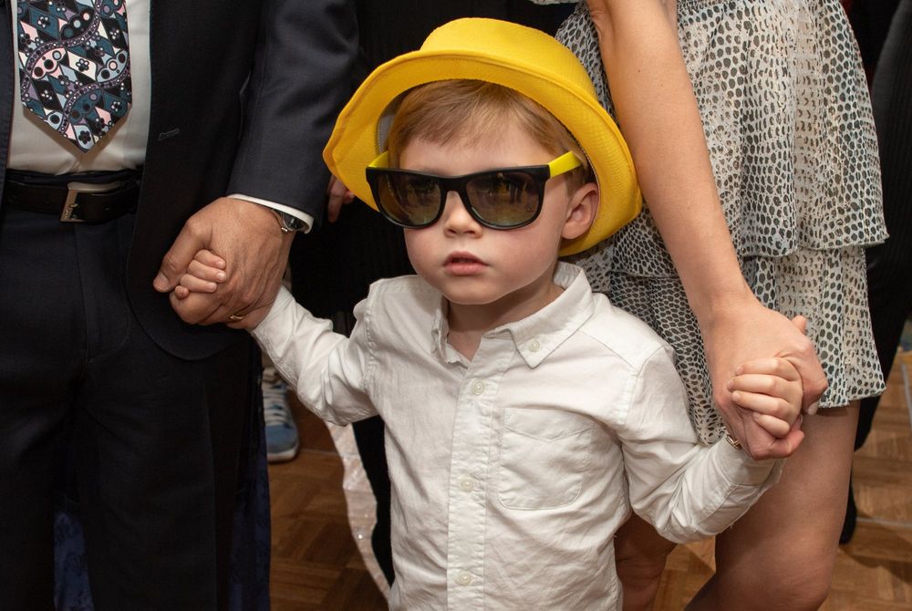 Young guest in yellow hat and sunglasses at formal event with party decorations.