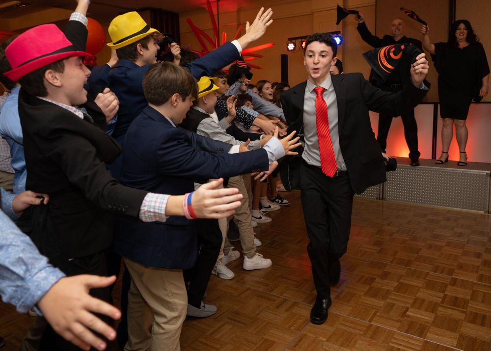 Dancers in formal wear moving energetically on a wooden dance floor at an indoor celebration.
