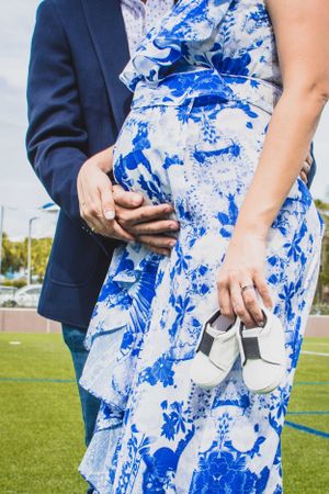 A couple in formal attire poses on a soccer field, with the person wearing a blue and white patterned dress.