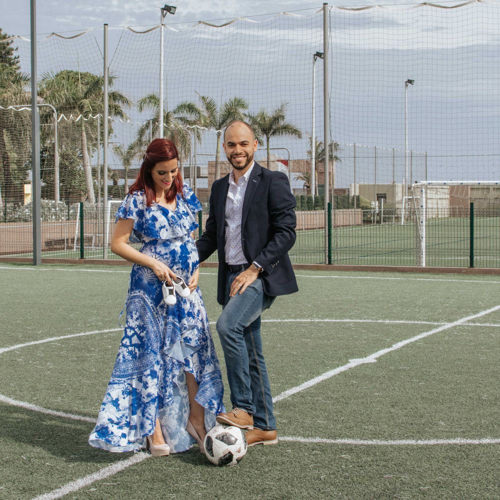 A playful couple poses with a soccer ball on a sports field wearing formal attire.