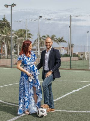 A couple plays with a soccer ball on an artificial turf field wearing formal clothes.