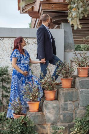 A couple walks up stone steps past terracotta planters in a garden setting.