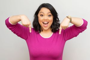Woman in pink top and dark hair poses with animated expressions against gray background.