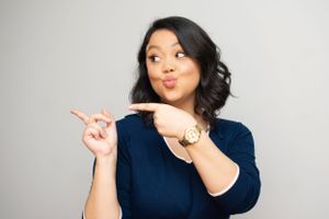 Woman in navy blue shirt making playful gestures and expressions in studio setting.