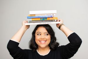 Woman balancing books on head while making playful expressions in studio.