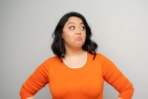 Someone in an orange top poses with hands on hips while looking up skeptically.