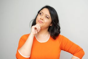 Someone in an orange sweater strikes a thoughtful pose with finger on chin.