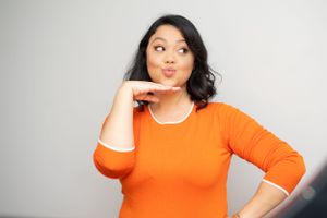 Someone in orange making a silly face while posing against gray background.