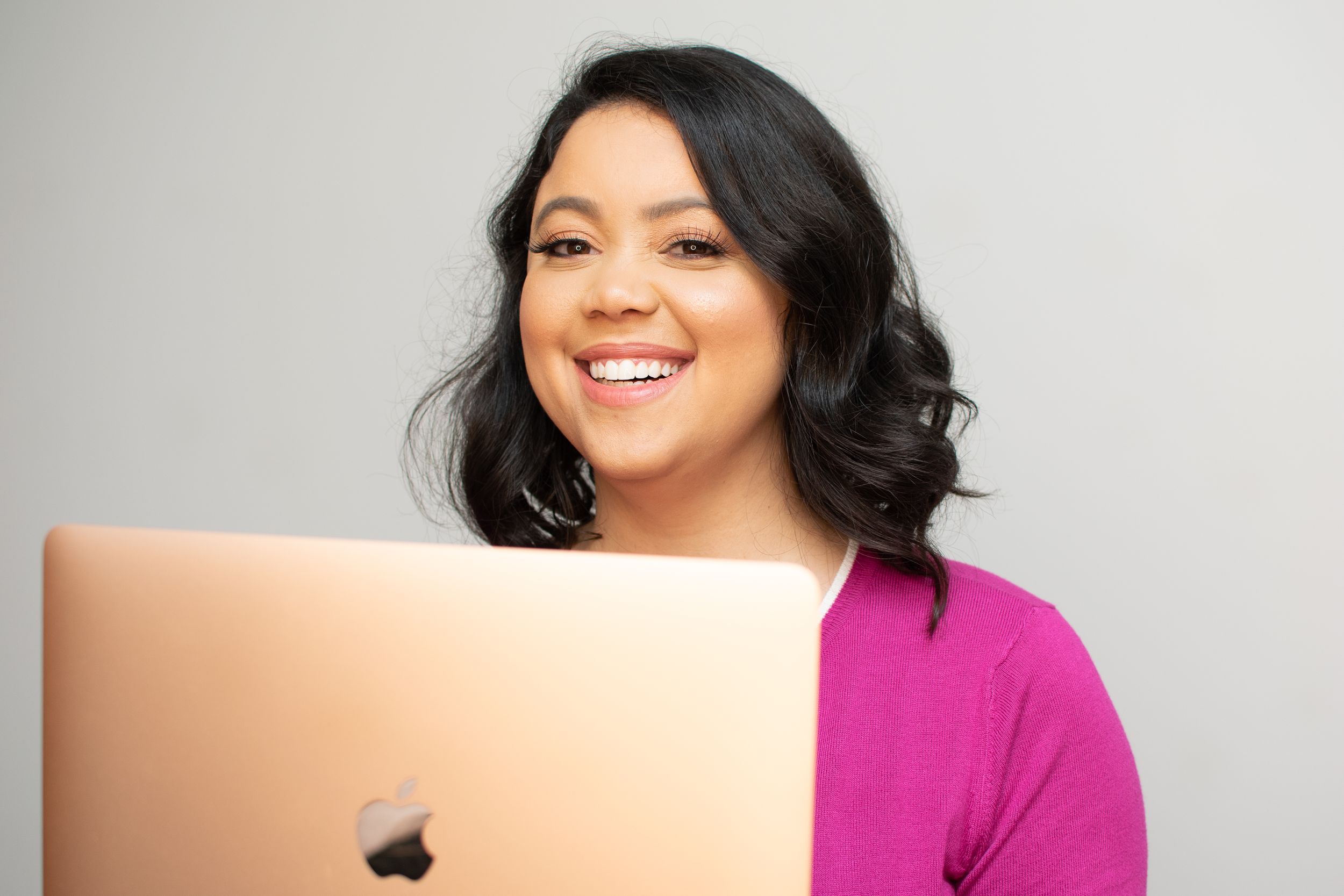 Someone in bright clothing smiles while working on a laptop computer.