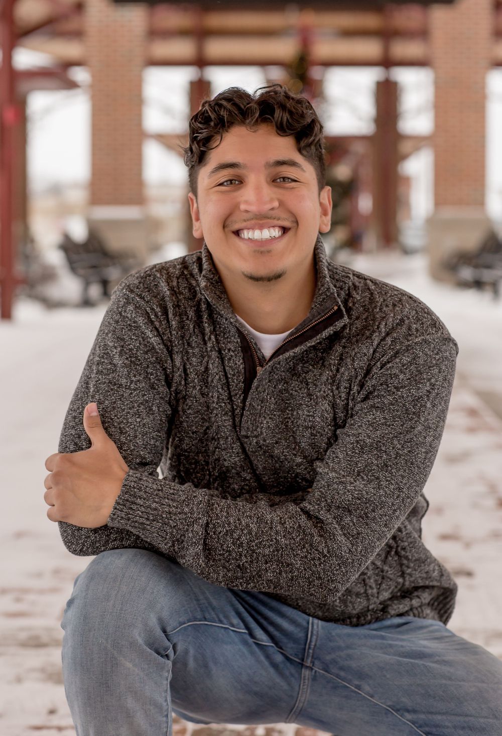 Young man in gray sweater sitting outdoors in snow smiling confidently.