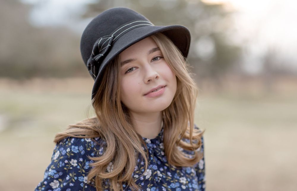 Young woman wearing dark floral dress and gray cloche hat outdoors.