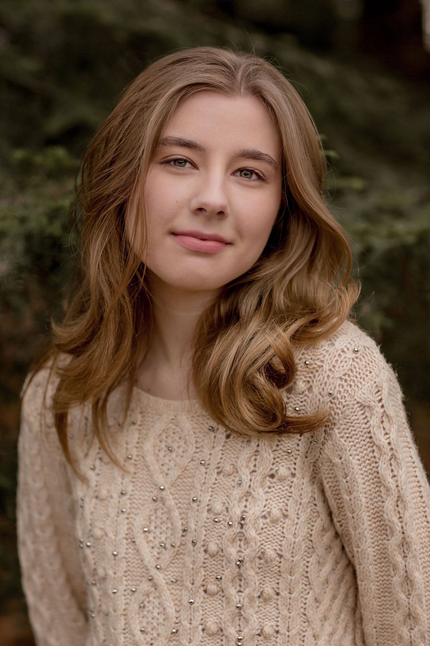 Teen girl with wavy blonde hair in cream knit sweater outdoor portrait.