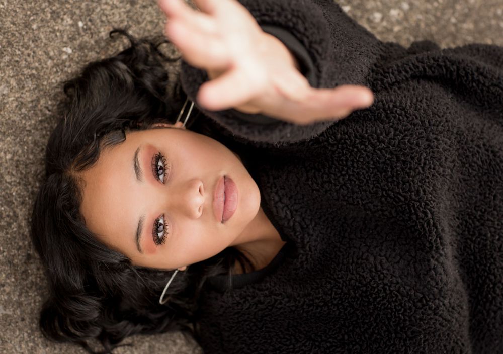 Young woman in black fleece jacket lying on ground reaching toward camera.