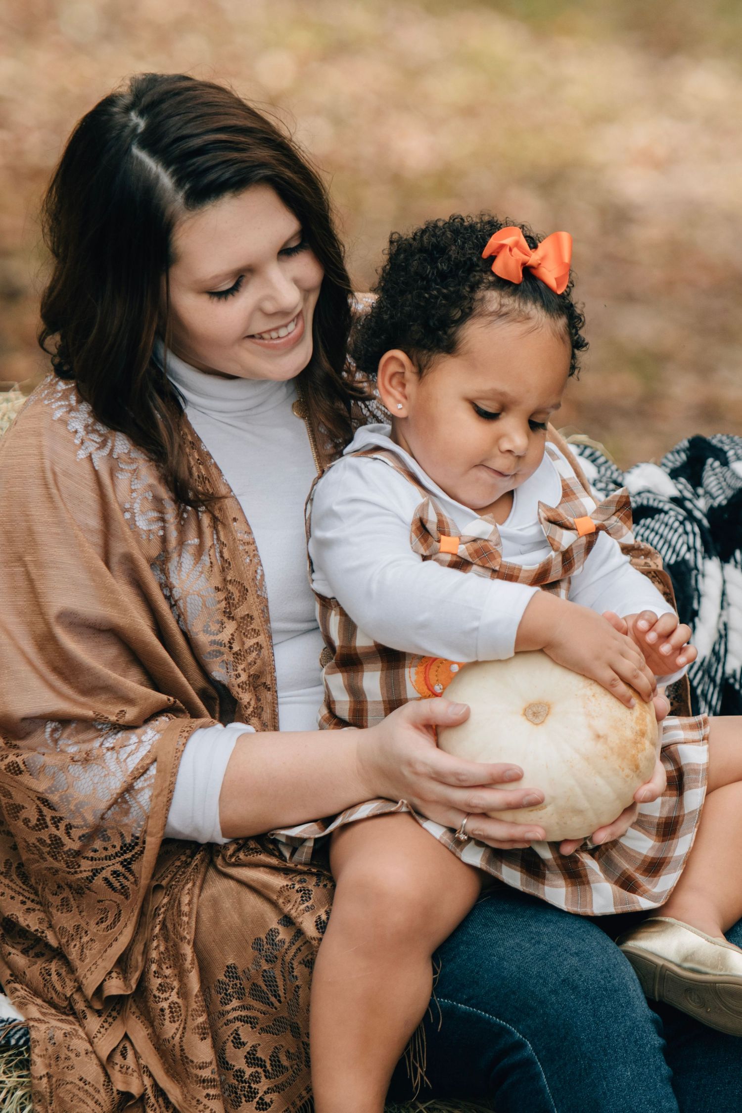 Children play with white pumpkin while sitting together on ground during fall season.