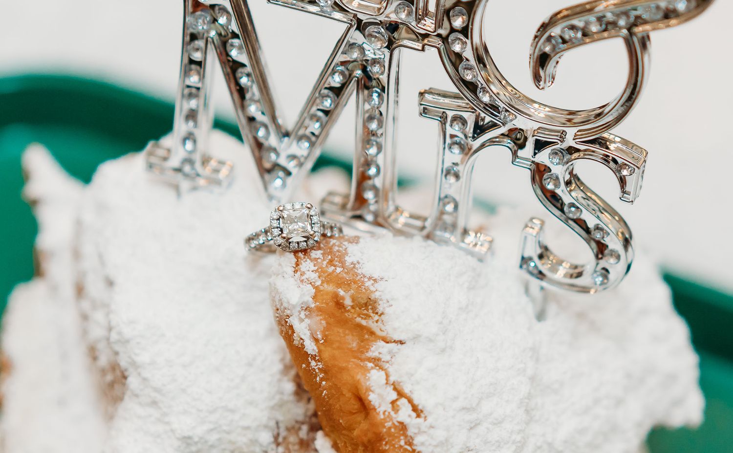 A diamond ring sits on top of a pile of beignets with a 'Mr. and Mrs.' sign next to it on a table in Cafe du Monde.