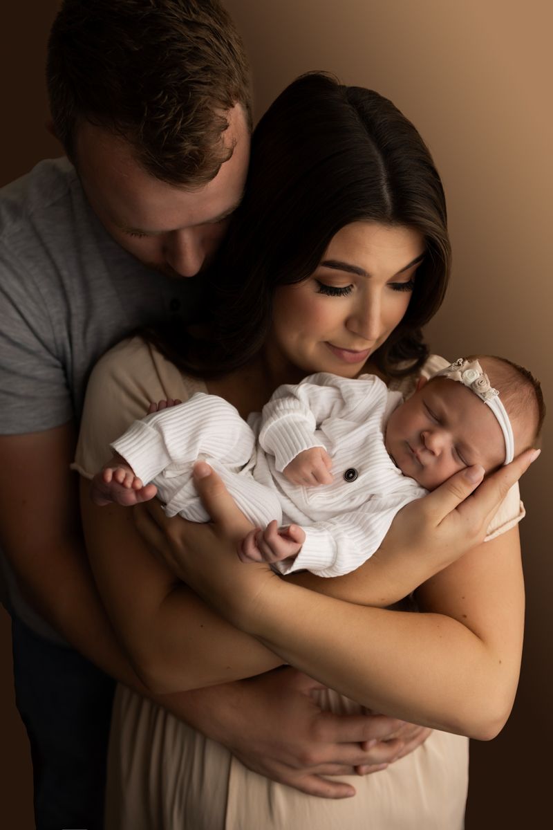 Newborn baby girl in white onesie, being held by her mother and father.