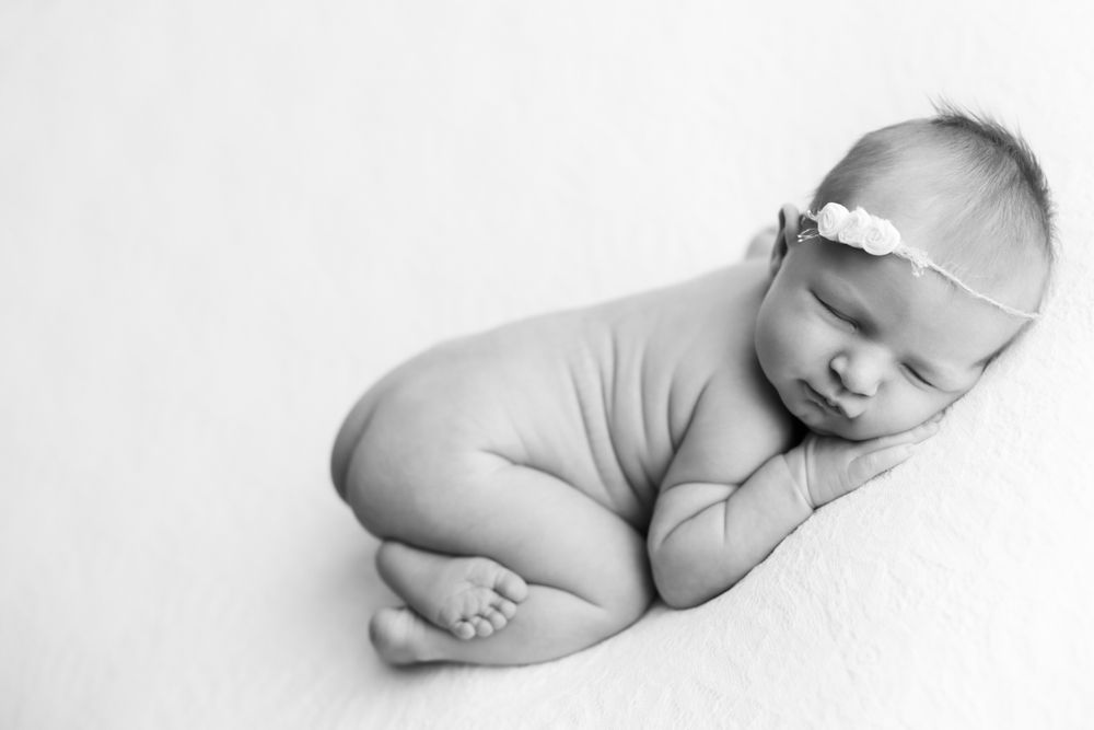 Black and white image of newborn baby girl cuddled on her hands and knees in a white floral headband.