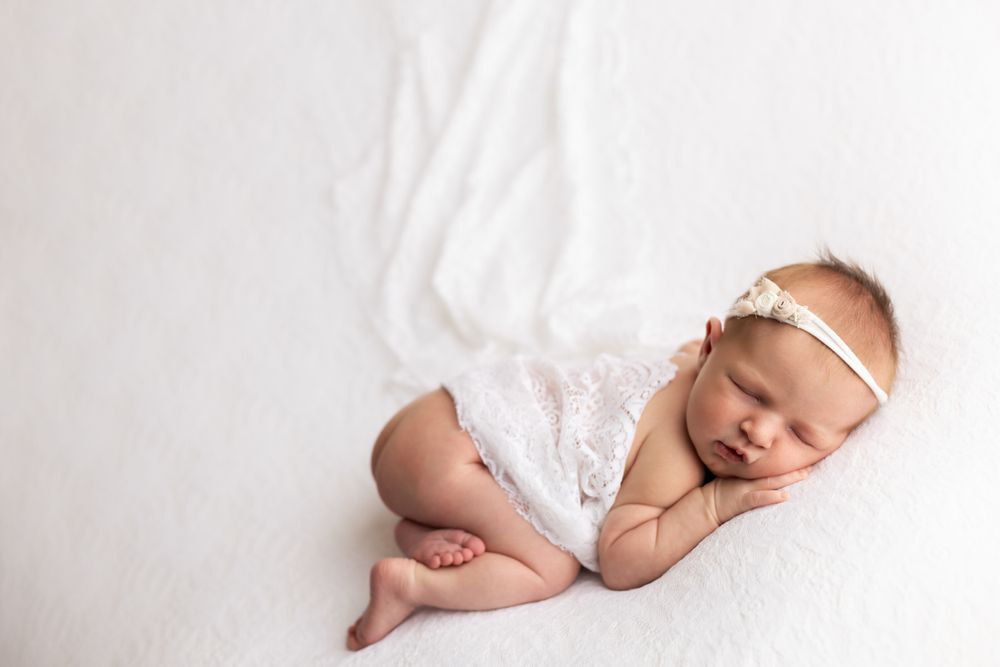 Newborn baby girl cuddled on her hands and knees with blanket over her back.