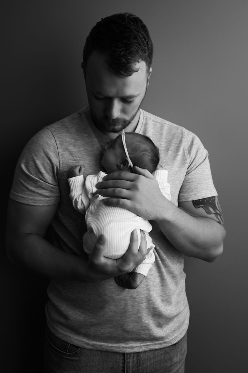 Black and white image of newborn baby girl cuddled on her dad's chest.