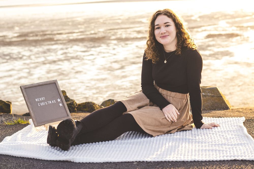 Someone sits on white blanket at beach with letterboard during sunrise.