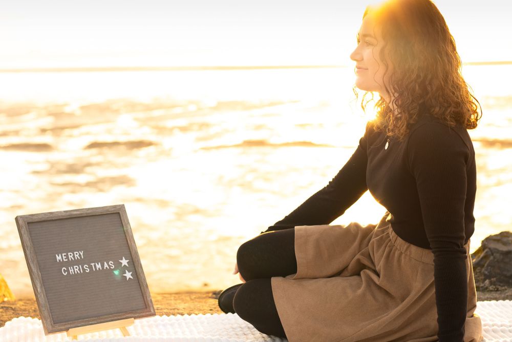 A person sits peacefully by the ocean at sunrise with a letter board.