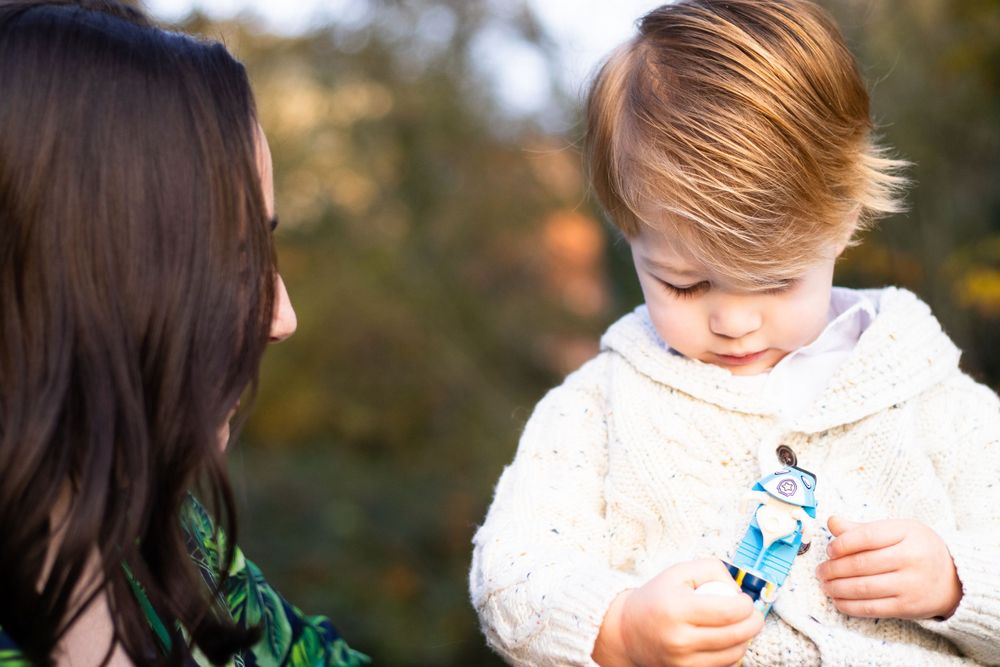 Child in white sweater looks down at small toy.