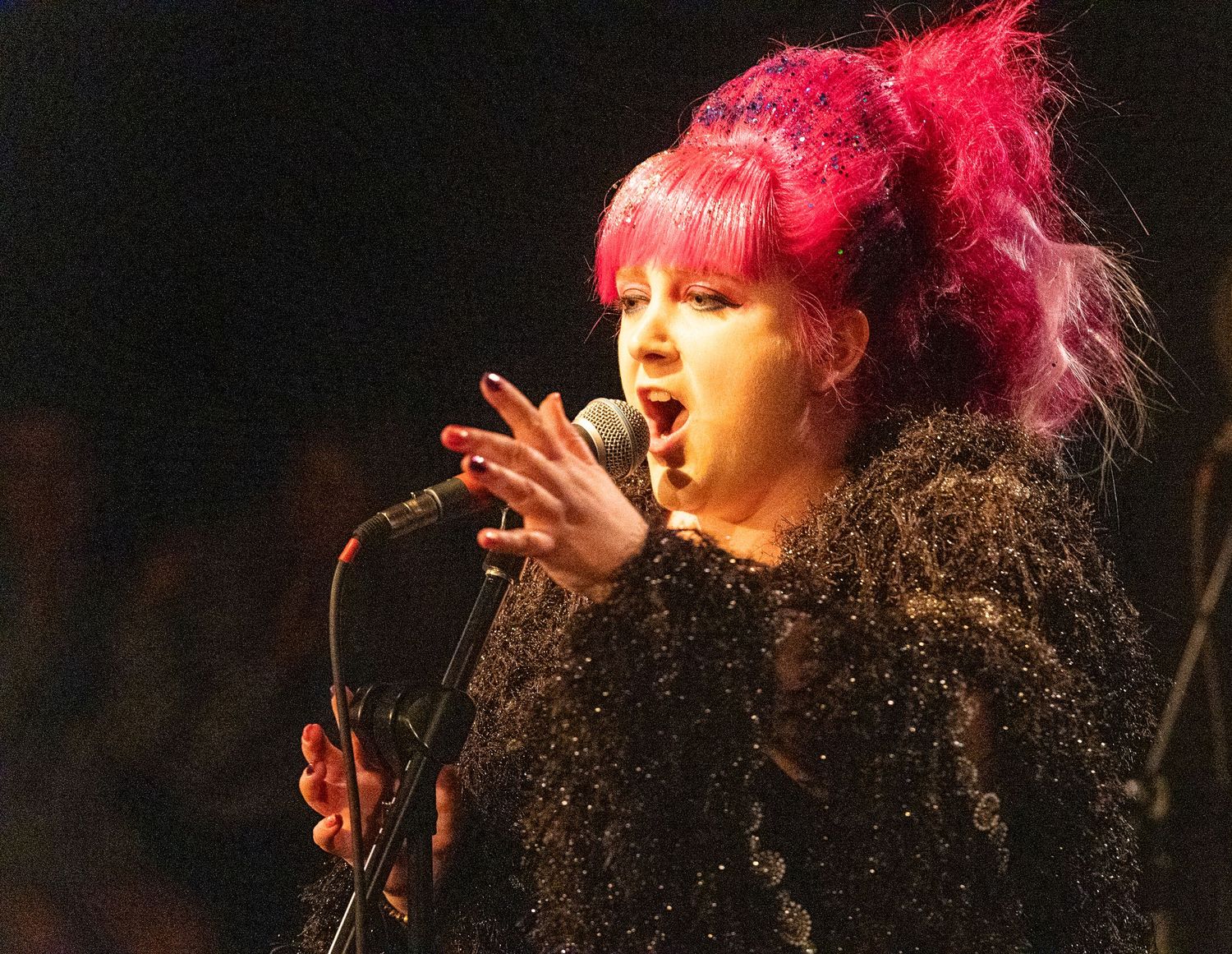 A singer with bright red hair performs passionately on stage with microphone.