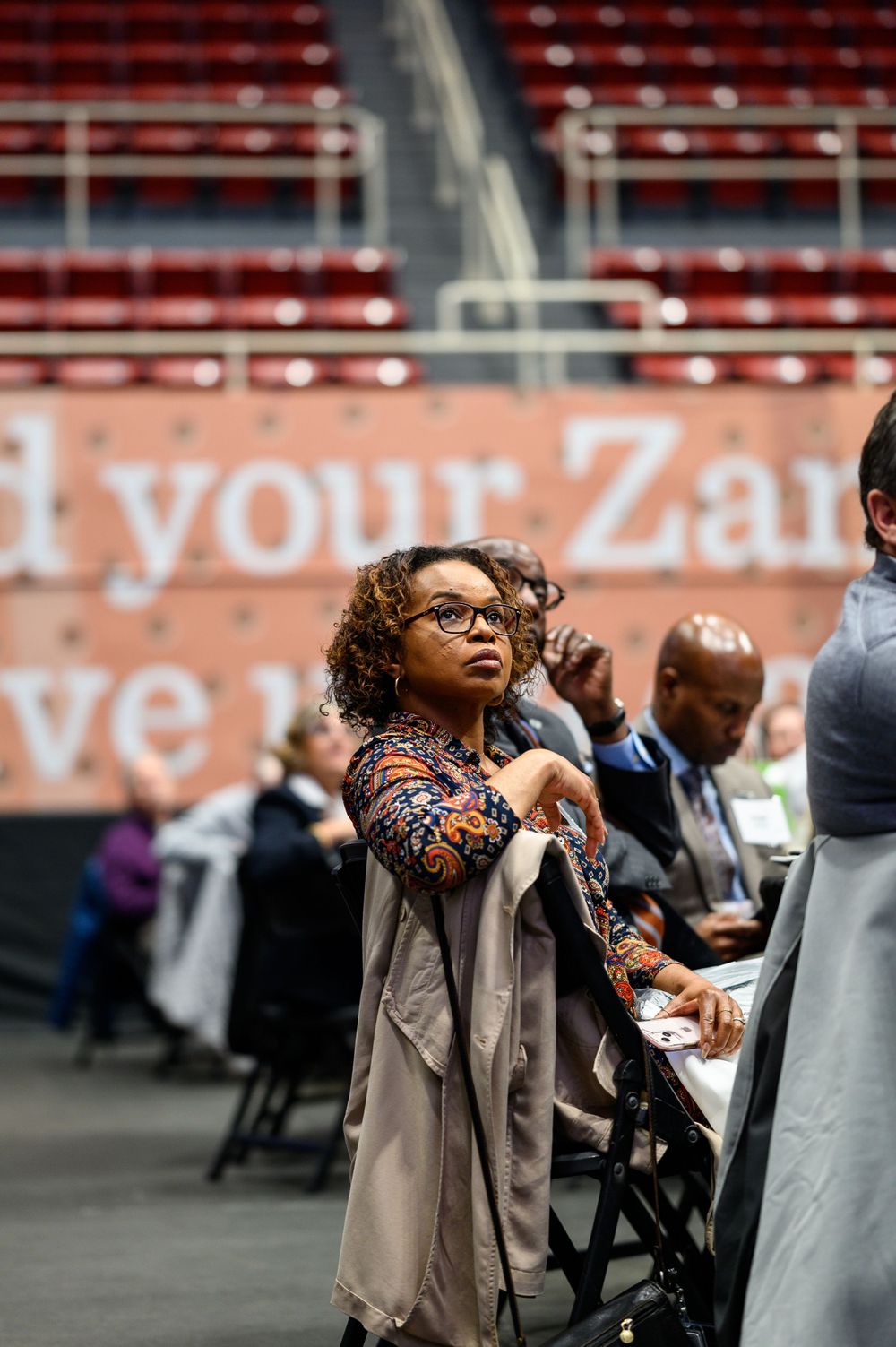 Event attendees in conversation during a gathering in an arena with red seats visible.